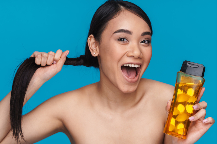 Mulher sorridente segurando o cabelo e um frasco de shampoo sem sal