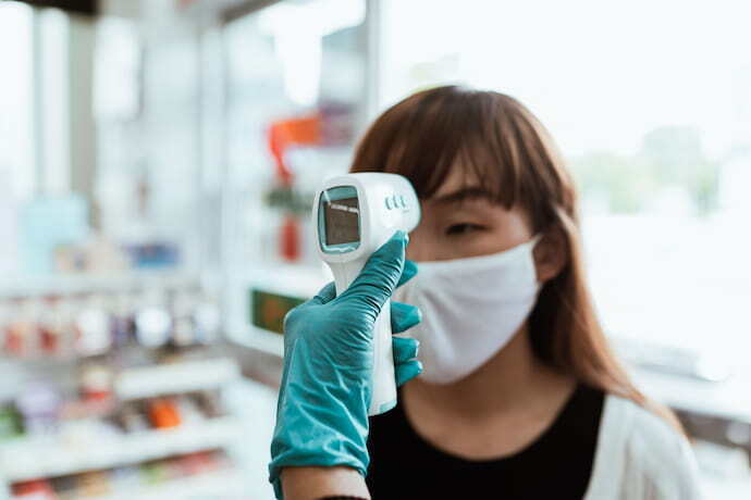 Mulher usando máscara de proteção, tendo a temperatura aferida. 