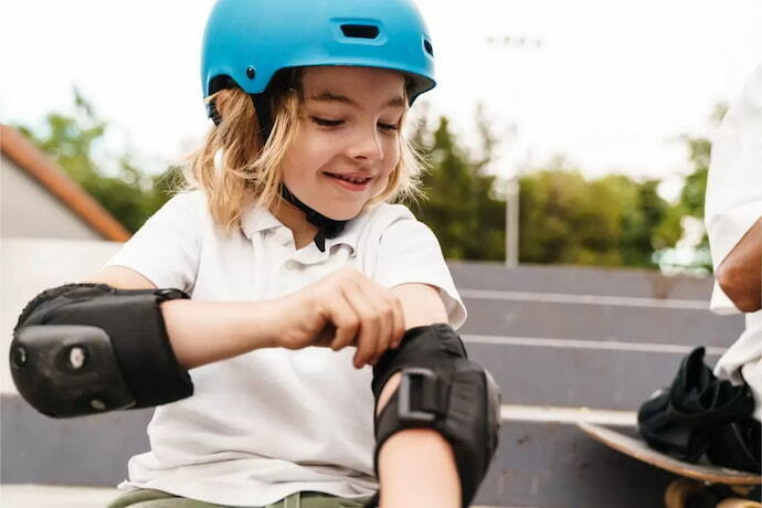 Menina com capacete azul, ajustando cotoveleiras